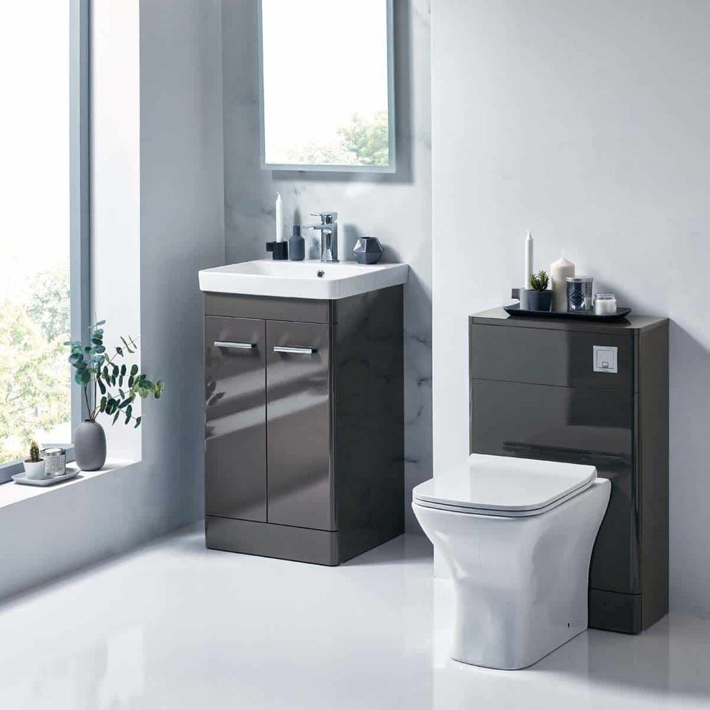 Modern grey bathroom vanity with integrated sink and sleek storage cabinets, next to a contemporary toilet, decorated with candles and minimal accessories, bright natural light streaming through a large window, creating a stylish and functional bathroom space.