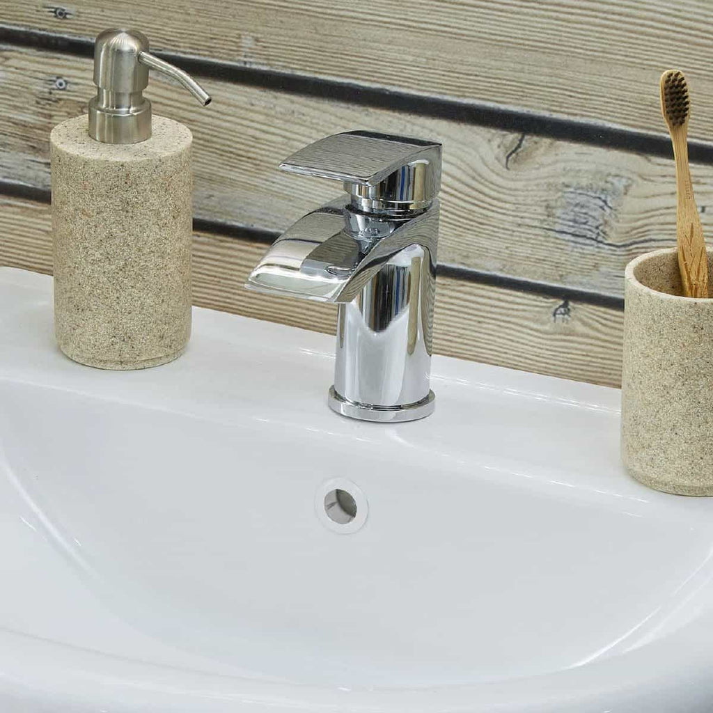 Shiny chrome bathroom sink tap with beige stone soap dispenser and toothbrush holder against a wooden wall. Perfect for modern bathroom upgrades and eco-friendly hygiene.