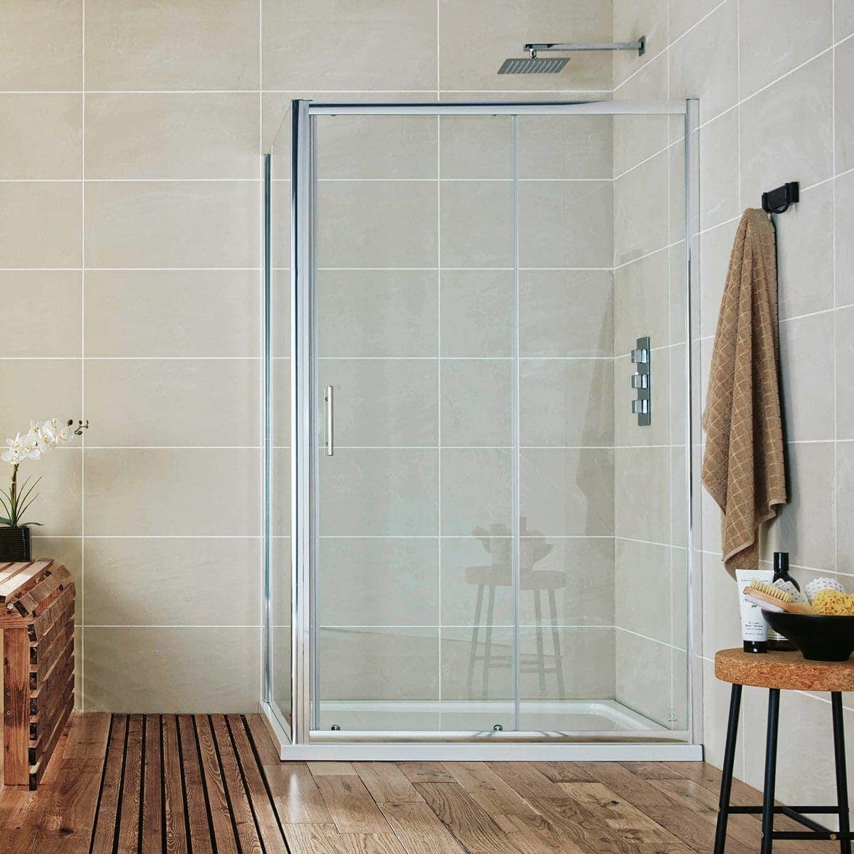 Shower enclosure with glass doors and modern controls in a contemporary bathroom with beige tiled walls and wooden floor tiles, featuring a towel hook and small side table with toiletries, designed for stylish bathing spaces.