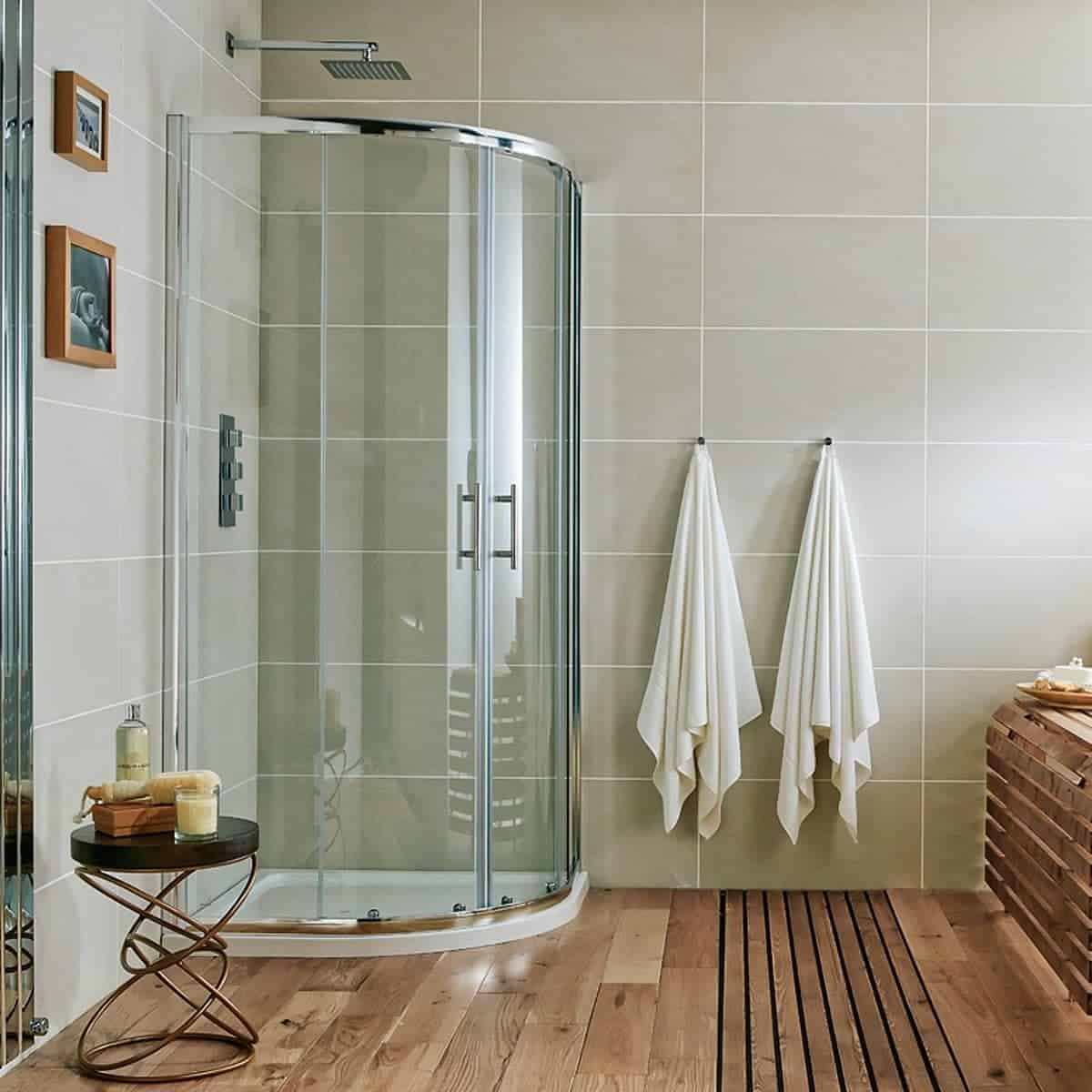 Metaphorically, it's a modern, beige-tiled walk-in shower with glass enclosure, two white towels hanging on hooks, and wooden accents, exemplifying contemporary bathroom design.