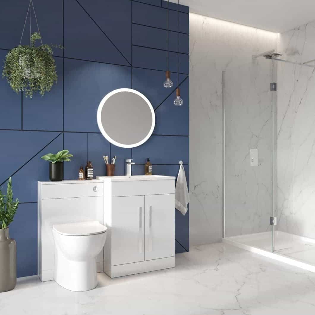 Modern bathroom with white vanity unit and toilet, blue accent wall with geometric paneling, round mirror, glass shower enclosure, and marble flooring, showcasing contemporary bathroom fixtures and decor.