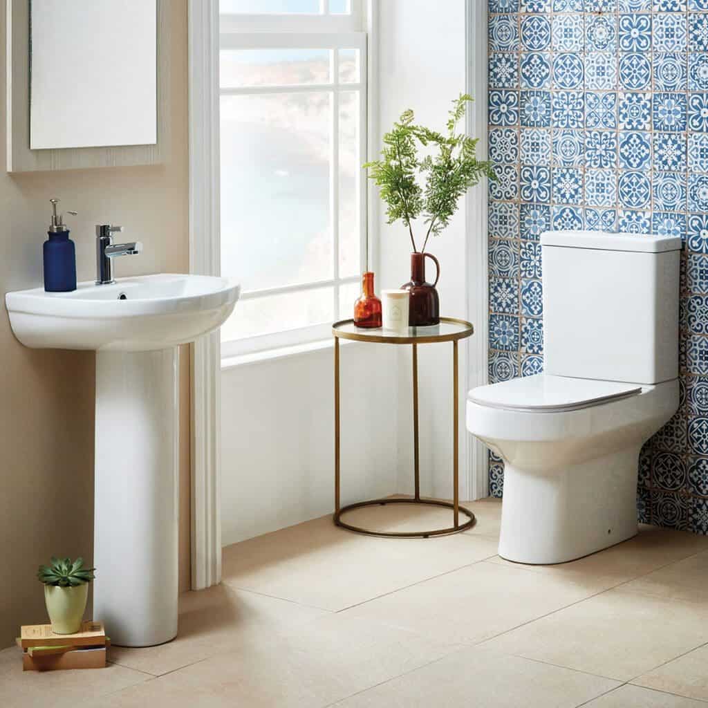 Elegant bathroom with modern white toilet and wall-mounted sink, featuring blue patterned tiles, natural light, and decorative accessories, showcasing stylish and functional bathroom design.