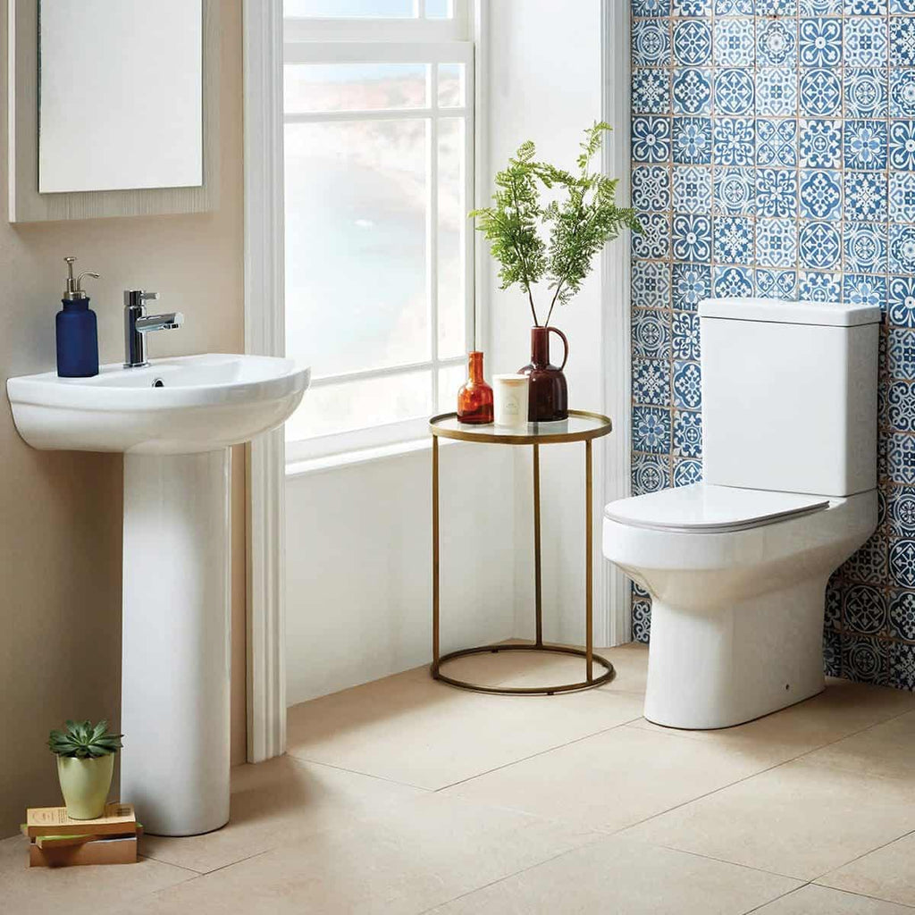 Elegant modern bathroom with white sink, toilet, decorative blue patterned tiles, natural light, and stylish accessories for a fresh, contemporary look.