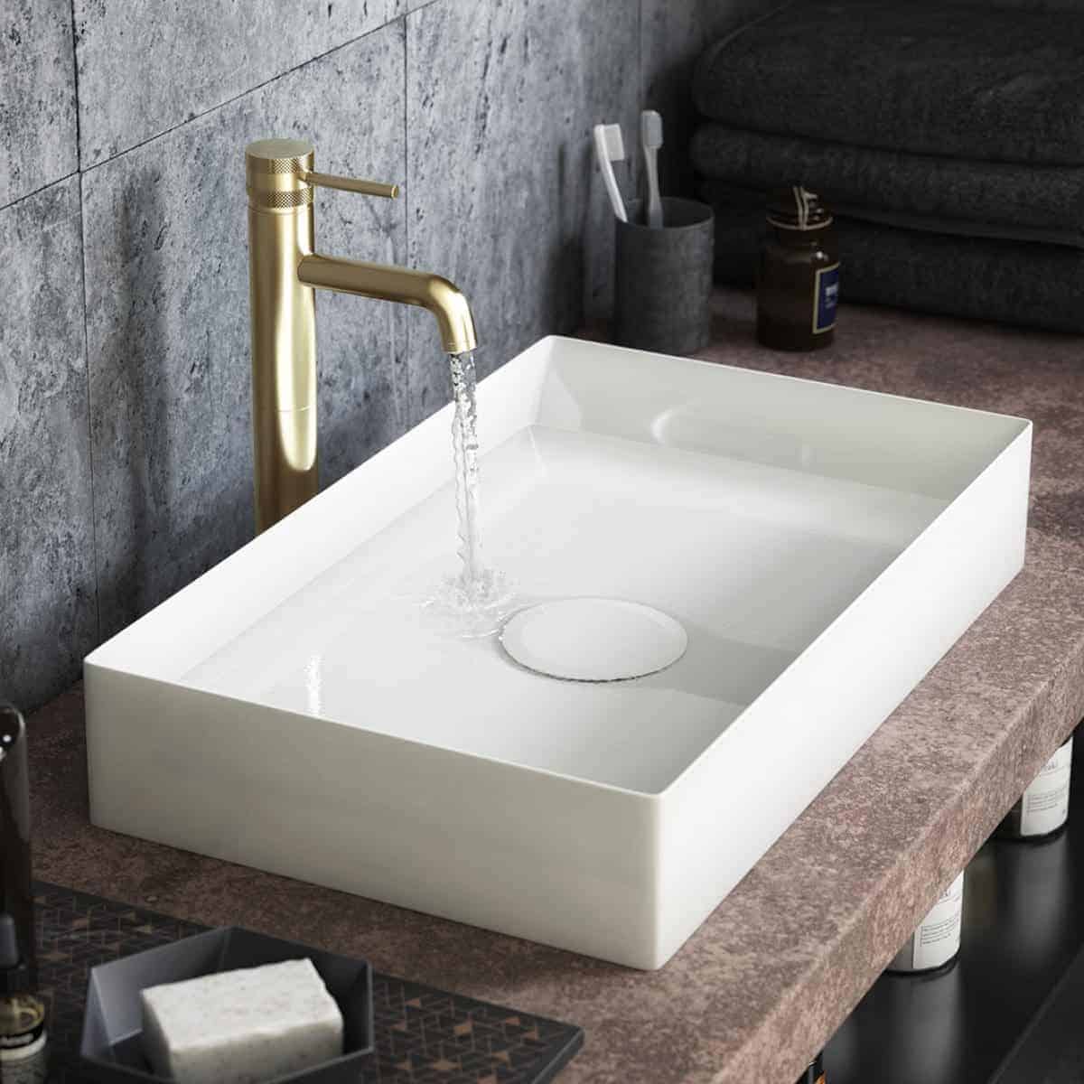 Sleek modern bathroom sink with a gold tap and flowing water, set on a stone countertop. Perfect for contemporary bathroom designs, combining functionality with elegant style.