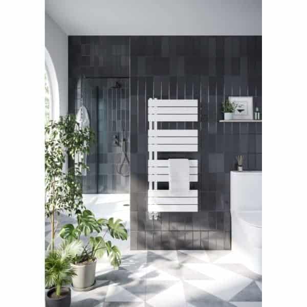 Modern bathroom with black tiled walls, white towel radiator, and shower area featuring a glass partition, complemented by green indoor plants and minimalist decor, creating a sleek and stylish space.
