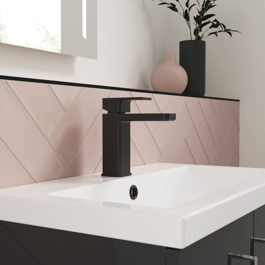 Modern black bathroom tap on white sink with pink tiled backsplash, minimalist bathroom decor, and stylish vases on the countertop for contemporary bathroom design.