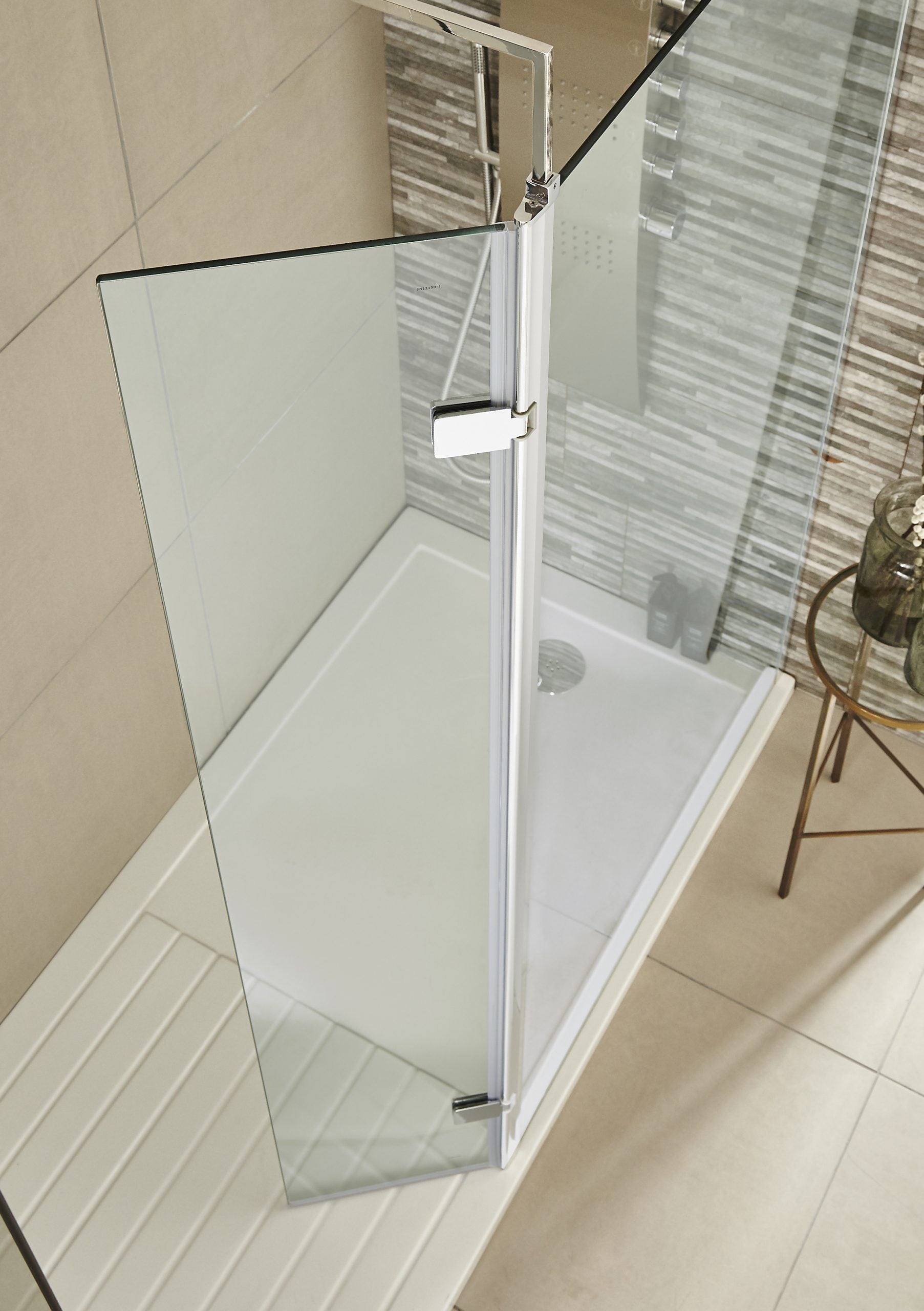 Glass shower enclosure with chrome handle and frame, installed on a beige tiled bathroom floor.