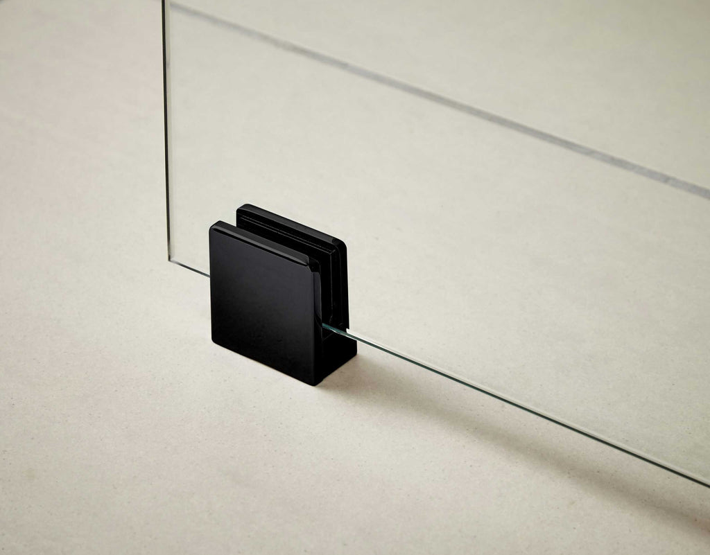 Sealed glass shower door hinge with black aluminium housing on a neutral background, showcasing modern bathroom hardware.