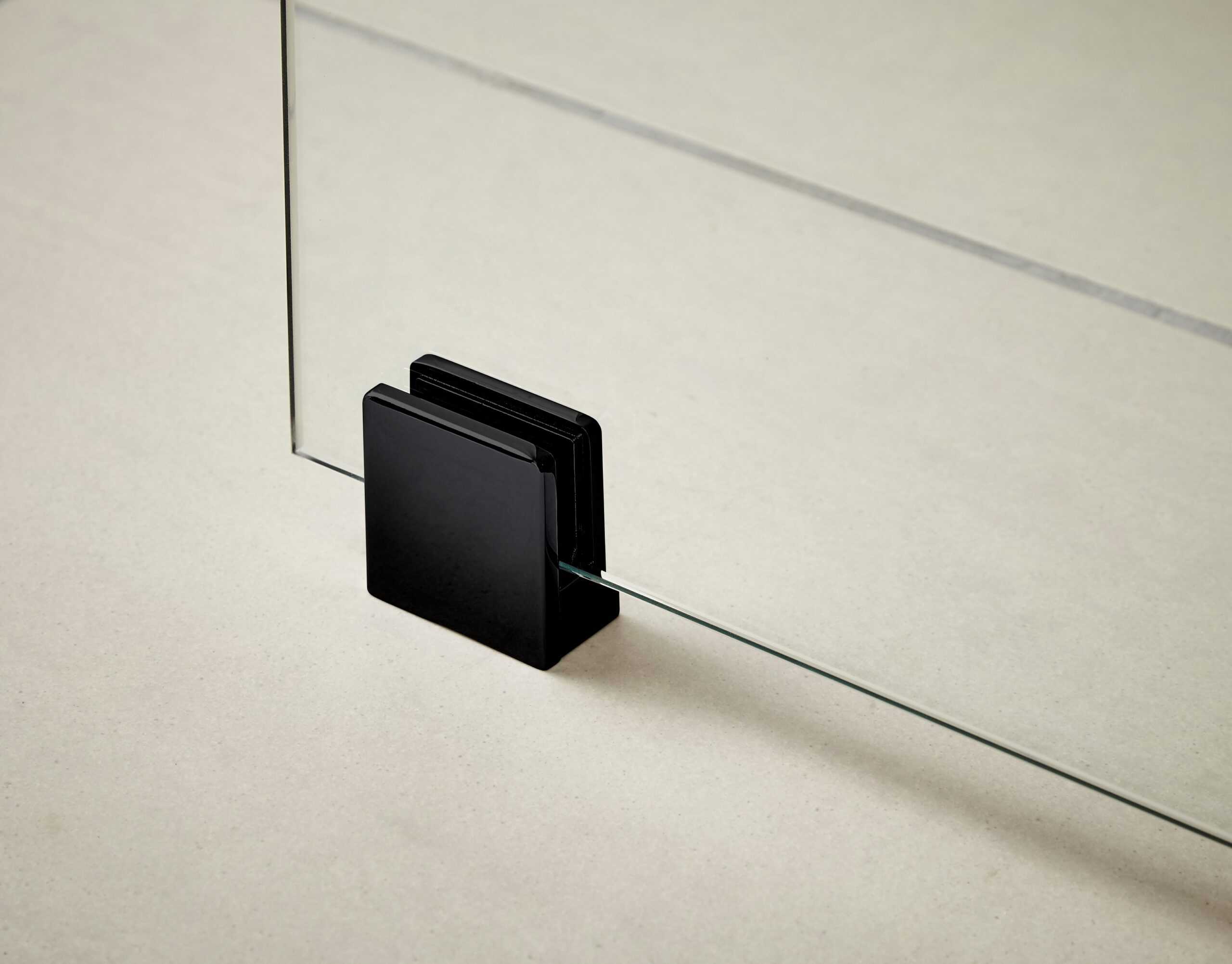 Sealed glass shower door hinge with black aluminium housing on a neutral background, showcasing modern bathroom hardware.